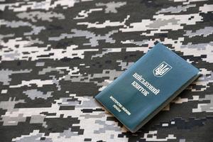 SUMY, UKRAINE - MARCH 20, 2022 Ukrainian military ID on fabric with texture of pixeled camouflage. Cloth with camo pattern in grey, brown and green pixel shapes with Ukrainian army personal token photo