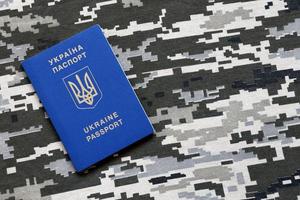 Ukrainian foreign passport on fabric with texture of military pixeled camouflage. Cloth with camo pattern in grey, brown and green pixel shapes and Ukrainian ID photo