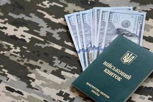 Ukrainian military ID and US dollar bills on fabric with texture of pixeled camouflage. Cloth with camo pattern in grey, brown and green pixel shapes with Ukrainian army personal token. photo