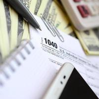 The pen, notebook, calculator, smartphone and dollar bills is lies on the tax form 1040 U.S. Individual Income Tax Return. The time to pay taxes photo