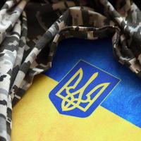 Ukrainian flag and coat of arms with fabric with texture of pixeled camouflage. Cloth with camo pattern in grey, brown and green pixel shapes with Ukrainian trident sign photo