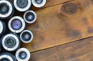 Several photographic lenses lie on a brown wooden background. Space for text photo