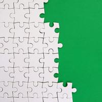 Fragment of a folded white jigsaw puzzle on the background of a green plastic surface. Texture photo with copy space for text