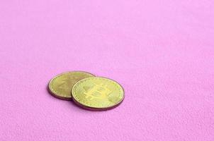 dos bitcoins dorados se encuentran sobre una manta hecha de suave y esponjosa tela de lana rosa claro. visualización física de moneda criptográfica virtual foto