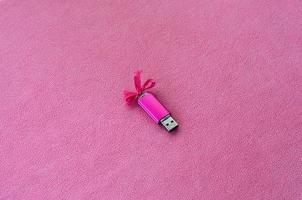 la tarjeta de memoria flash usb de color rosa brillante con un lazo rosa yace sobre una manta de suave y peluda tela de vellón rosa claro. diseño clásico de regalo femenino para una tarjeta de memoria foto