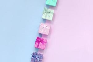 Small gift boxes of different colors with ribbons lies on a violet and pink background photo