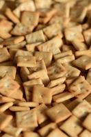 A lot of small cookies are square shaped. A pattern of a yellow salt cracker. Background image with salted pastry photo