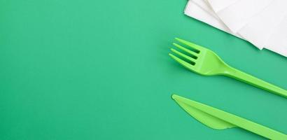 cubiertos desechables de plastico verde. el tenedor y el cuchillo de plástico yacen sobre una superficie de fondo verde junto a las servilletas foto