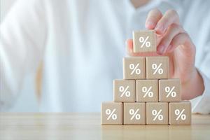 Interest rate finance and mortgage rates. Hand holding percentage sign on wooden cube from stack of blocks, financial growth, interest rate increase, inflation, sale price and tax rise concept. photo