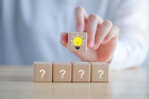 Idea and creativity concept. Creative process concept and problem solution. hand holding glowing light bulb idea from many question mark on wooden block. photo