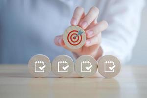 Checklist, Task list, Survey and assessment, Quality Control, Goals achievement and business success. to do list, Hand holding dartboard icon and checklist with check mark icon on wooden blocks. photo