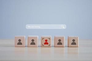 Business hiring and recruitment selection. Career opportunity. Human Resource Management. Magnifier glass on search bar with We are hiring text and red human icon among many human on wooden block. photo