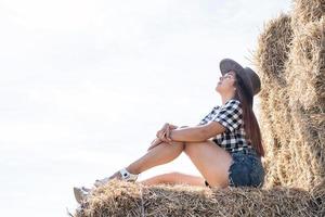 beautiful woman in plaid shirt and cowboy hat resting on haystack photo