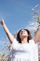 alegre mujer caucásica vestida de blanco en la cosecha de maíz, fondo del cielo foto