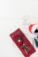 Christmas table setting with white dishware, silverware and red and green decorations on white wooden background. Top view. photo