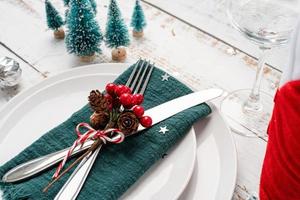 Christmas table setting with white dishware, silverware and red and green decorations on white wooden background. High angle view. photo