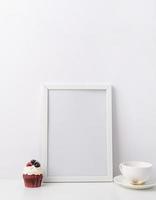 Art photo frame mockup with cup of coffee and cupcake, white background