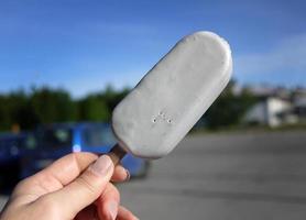 A hand holding popsicle ice cream stick Champagne flavor in hand, on summer , blurry background blue sky, copy space photo