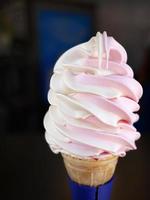 Close up a two color pink white soft cream in waffle cone on summer, with dark blurry background, copy space photo