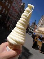 Close up a hand holding tall twist shape soft cream in waffle cone on summer, blurry background of old town photo