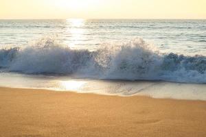 olas del mar golpeando la playa con puesta de sol foto