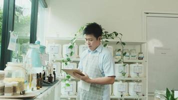 Asiatischer männlicher Ladenbesitzer überprüft den Bestand an natürlichen Bio-Produkten in der Schaufensterauslage im Nachfüllladen, abfallfreies und plastikfreies Lebensmittel, umweltfreundliche, nachhaltige Lebensstile, wiederverwendbarer Laden. video