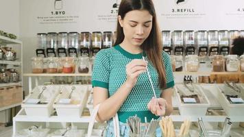 A young Caucasian female customer chose usable and recycled straws, shopping for organic products in refill store, zero-waste grocery, and plastic-free, environment-friendly, sustainable lifestyles.