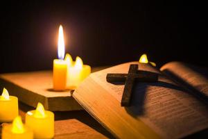 velas encendidas con la sagrada biblia y la cruz o el crucifijo sobre un fondo de madera antiguo en la iglesia. luz de las velas y libro abierto sobre una mesa de madera vintage estudio y lectura del cristianismo en el hogar. concepto de la religión de cristo foto