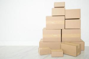 pila de cajas de cartón para mudanzas, habitación vacía con una pared blanca y cajas de cartón con código de barras sin marca en el suelo. entrega de mercancías, compras. cajas de cartón sobre fondo de pared gris. foto