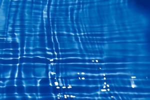 Defocus blurred transparent blue colored clear calm water surface texture with splash, bubble. Shining blue water ripple background. Surface of water in swimming pool. Blue bubble water shining. photo