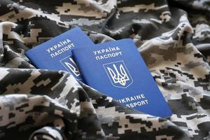 SUMY, UKRAINE - MARCH 20, 2022 Ukrainian foreign passport on fabric with texture of military pixeled camouflage. Cloth with camo pattern in grey, brown and green pixel shapes and Ukrainian ID photo