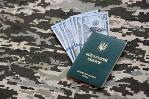 SUMY, UKRAINE - MARCH 20, 2022 Ukrainian military ID and US bills on fabric with texture of camouflage. Cloth with camo in grey, brown and green pixel shapes with Ukrainian army personal token. photo