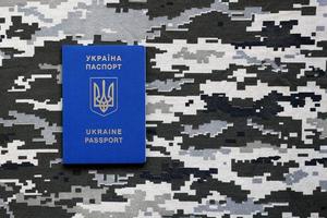 SUMY, UKRAINE - MARCH 20, 2022 Ukrainian foreign passport on fabric with texture of military pixeled camouflage. Cloth with camo pattern in grey, brown and green pixel shapes and Ukrainian ID photo