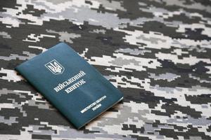 SUMY, UKRAINE - MARCH 20, 2022 Ukrainian military ID on fabric with texture of pixeled camouflage. Cloth with camo pattern in grey, brown and green pixel shapes with Ukrainian army personal token photo