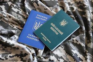 SUMY, UKRAINE - MARCH 20, 2022 Ukrainian military ID and foreign passport on fabric with texture of pixeled camouflage. photo