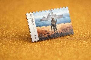 TERNOPIL, UKRAINE - SEPTEMBER 2, 2022 Famous Ukrainian postmark with russian warship and ukrainian soldier as wooden souvenir on golden glitter background photo