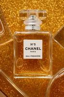 TERNOPIL, UKRAINE - SEPTEMBER 2, 2022 Chanel Number 5 Eau Premiere worldwide famous french perfume bottle among other perfumes on shiny glitter background in yellow colors photo