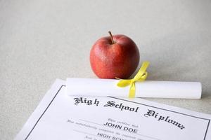 A high school diploma lies on table with small scroll and red apple. Education documents photo
