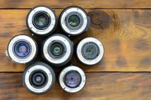 Several photographic lenses lie on a brown wooden background. Space for text photo