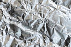 Thin wrinkled sheet of crushed tin aluminum silver foil background with shiny crumpled surface for texture photo