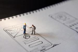 User Experience Concept. present by two Miniature Figure of Businessman standing on Paper of Interface Design Sketch at Night. Overtime Work photo