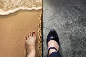 concepto de equilibrio de vida para el trabajo y los viajes presente en la posición de vista superior por la mitad de los zapatos de mujer trabajadora de negocios en el suelo de cemento y descalzo en la playa de arena foto