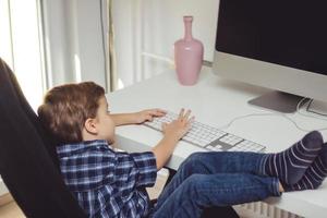 niño pequeño escribiendo en el teclado mientras usa la computadora de escritorio en casa. foto