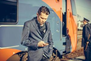 hombre de negocios revisando el horario en el teléfono móvil en la estación de tren. foto