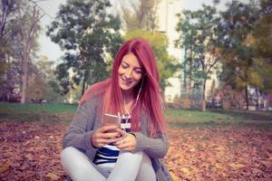 Happy redhead woman listening favorite music in the park. photo