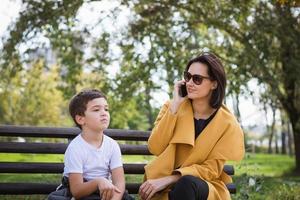 Mother talking on the phone while sitting with her son on park bench. photo