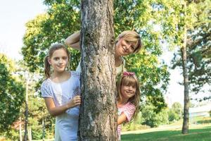 madre e hijas juguetonas que miran a escondidas detrás del árbol. foto