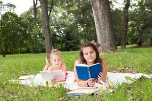 niñas pequeñas leyendo libros mientras se relajan en una manta en la naturaleza. foto