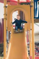 niño pequeño deslizándose en el patio de recreo. foto