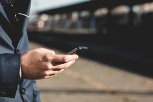 primer plano de hombre de negocios mediante teléfono móvil y estación de tren. foto